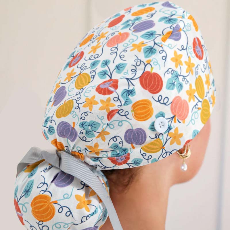 Ponytail scrub cap featuring pumpkin patterns, button detail, gray ribbon, modeled on a head